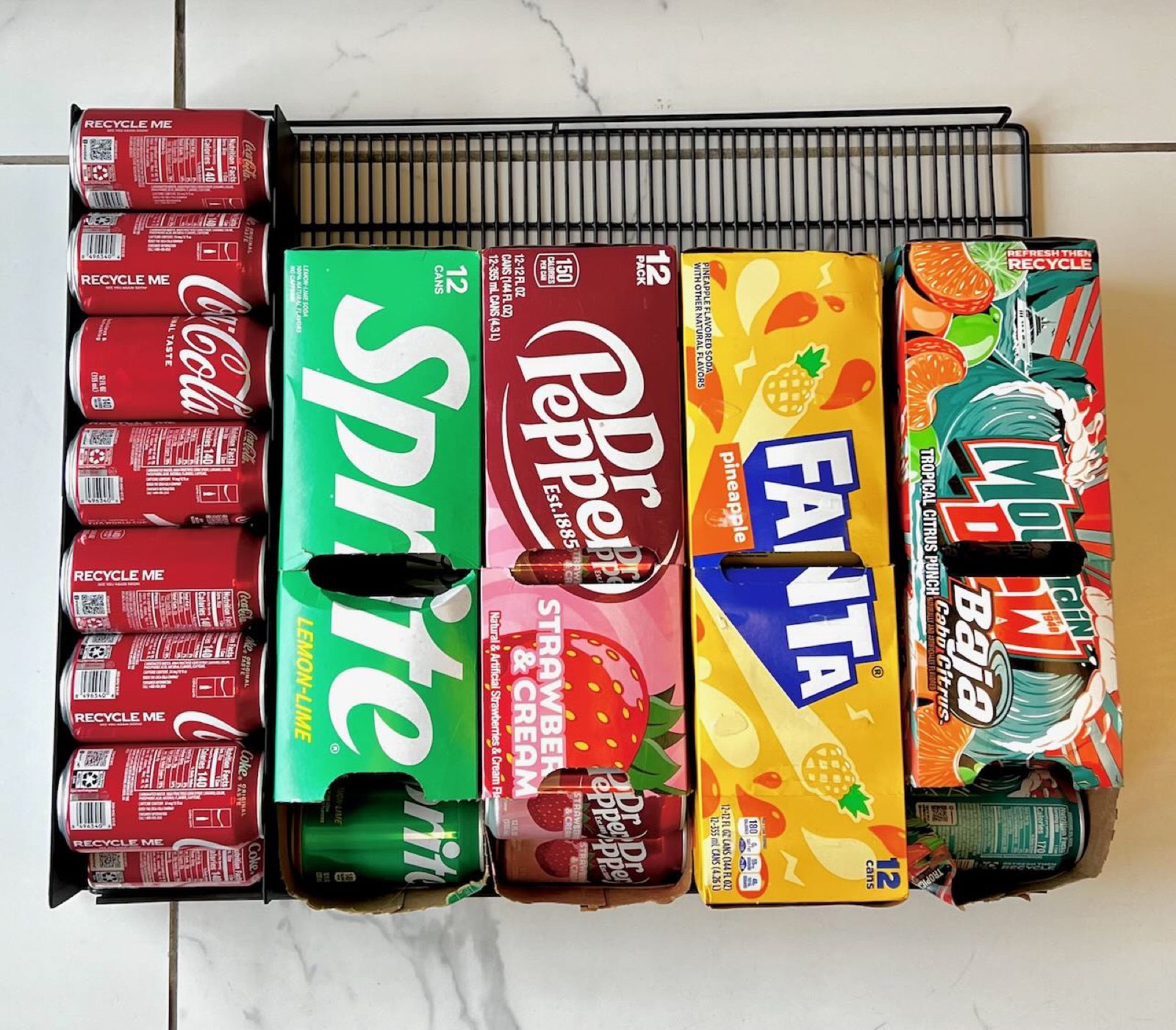 Top-down view of the rolling rack loaded with Coca-Cola cans on the left, next to four traditional 12-pack cardboard boxes on the right, in the same shelf footprint